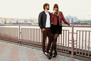 Full length  fashion image of  stylish couple in casual outfit, leather jacket and sunglasses standing on the bridge.   Handsome man with beard with his girlfriend spending romantic time together. photo