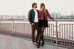 Full length  fashion image of  stylish couple in casual outfit, leather jacket and sunglasses standing on the bridge.   Handsome man with beard with his girlfriend spending romantic time together. photo