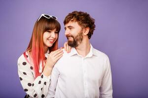 Cute couple hugging and looking on each other.  Handsome  man with beard and his pretty woman with pink hairs in stylish retro outfit posing on purple background in studio. photo