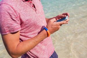 hombre participación móvil teléfono, mensajes de texto mensaje en su vacaciones increíble azul agua antecedentes. fiesta trabajar. foto