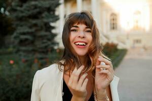 Blissful laughing woman playing with hairs and enjoing uotumn day in european city. Elegant look. photo