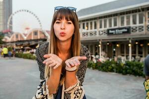 Young travel woman send kiss , having great time  on riverfront of Bangkok , ferris wheel  and  restaurants background. photo