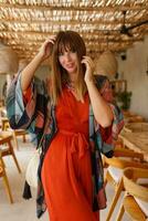 atractivo mujer en naranja de moda vestir posando en tropical cafetería. brillante atuendo. viaje y vacaciones Moda concepto. foto