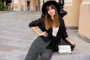 Confident stylish brunette woman   posing in  european city, walking on the street. Wearing casual outfit, black hat and blouse. Autumn fashion look. photo