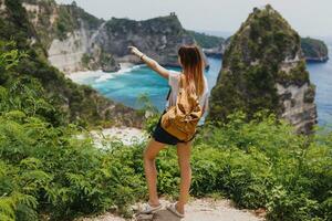 Back view of traveling  woman standing  on cliffs and tropical beach background. Freedom And adventure concept. Full length. Indonesia, Nusa Penida island. photo