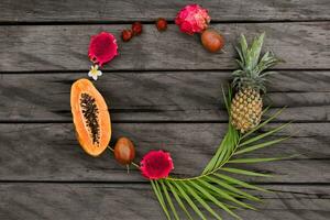 Creative round composition with tropical fruits on wood background, top view. Slices of papaya, dragon fruit and pineapple. Palm leave. Copy space, top view. photo