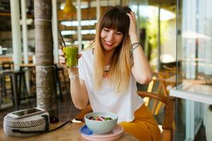 despreocupado sonriente mujer comiendo sano vegano desayuno. superalimentos cuenco coronado con chía, Granola y aguacate. moderno cafetería. bali estilo. foto