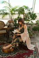 bohemio mujer en elegante hogar vestir leyendo libro en elegante vivo habitación. foto
