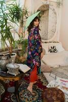 Woman with japanese umbrella popsing in  boho interior  with tropical plants and stylish furniture. photo