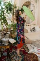 Woman with japanese umbrella popsing in  boho interior  with tropical plants and stylish furniture. photo