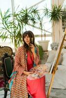 Portrait of beautiful artist woman in bohemian outfit posing with brush and palette in her art studio. photo