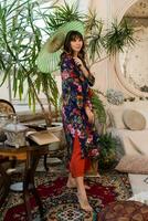 Woman with japanese umbrella popsing in  boho interior  with tropical plants and stylish furniture. photo