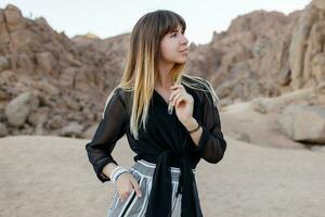 Elegant brunette woman  posing  in the Egyptian  desert sand dunes. Cliffs and mountains on background. Wearing black blouse and striped pants. photo