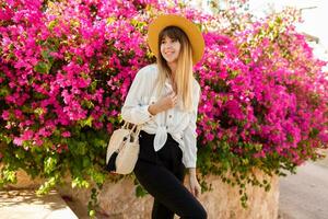 Pretty brunette woman in straw hat posing over pink blooming tree in sunny spring day. Holidays and shopping concept. photo