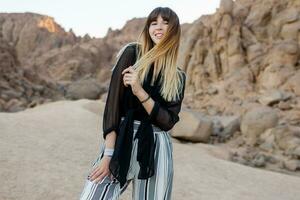 Pretty smiling fashionable girl posing  in the Egyptian  desert sand dunes. Cliffs and mountains on background. Wearing black blouse and striped pants. photo