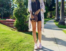 Fashion details  of stylish smiling woman   posing on exotic street near the hotel in sunny hot day. Spending her vacation in Los Angeles.  Holding mobile phone. Palm trees on background. photo