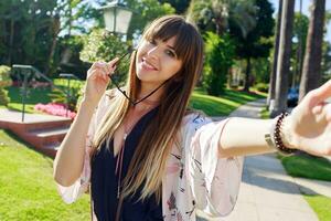 Beautiful long haired woman with  trendy hairstyle making self portrait by camera.  Green tropical park background. photo