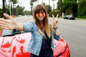 Cute woman in pink glasses making self portrait near amazing red convertible  sport car in California. photo