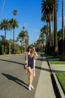 Full length  portrait of stylish smiling woman walking  on  exotic street near the hotel in sunny hot  day . Spending her vacation in Los Angeles photo