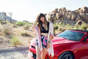 Brunette pretty seductive girl sitting on  red modern sport convertible car. Joshua tree national park background. photo