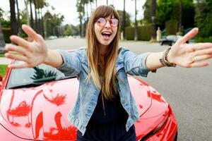 Cute   happy woman in pink glasses making self portrait near amazing red convertible  sport car in California. photo