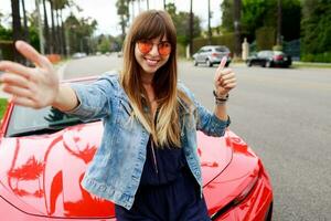 Cute woman in pink glasses making self portrait near amazing red convertible  sport car in California. photo