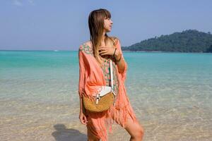 Seductive woman in boho beach dress with embroidery and tassel spending  her vacations on amazing beach in Thailand. photo