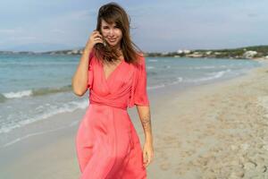 Seductive brunette woman  with tatoo on hand in pink dress posing on the beach. photo