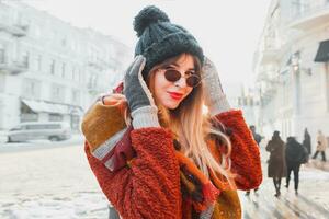 Winter   portrait of happy  woman walking  in knitted hat on sunny  street.  Smiling lady enjoying  weekends. Wearing stylish sunglasses and coat. photo