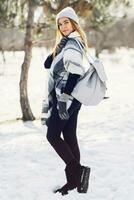 Winter lifestyle portrait of young blonde fresh lady in warm wool  fluffy  scarf and  hat with backpack. photo