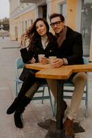 Fashionable couple in love sitting in street cafe  and drinking hot coffee while traveling in Europe. photo