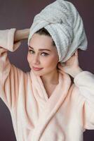 Arttractive smiling young woman wearing bathrobe and towel over her head standing  over pink background purple background. photo