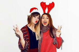 New year party. Two  beautiful girls  in funny masquerade Santa hats send kiss . Indoor stockpile image of best friends posing on white background. Isolate. photo