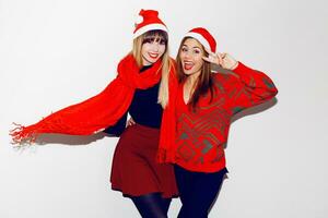 loco nuevo año fiesta humor. dos borracho riendo mujer teniendo divertido y posando en blanco antecedentes en linda mascarada sombreros. rojo suéter y bufanda. foto