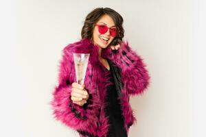 Happy  selebrating woman in stylish fur coat holding glass of shampagne , wearing pink fur coat and posing over white background. photo