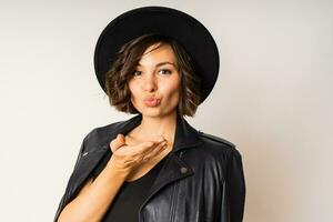 Elegant woman  in black hat, evening dress and leather jacket posing on white background in studio. photo