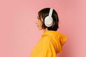 estudio foto de corto peludo morena mujer escuchando música por auriculares terminado rosado antecedentes. ver desde lado.