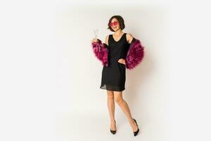 Happy  selebrating woman in stylish fur coat holding glass of shampagne , wearing pink fur coat and black party dress. posing over white background. Full lengt. photo