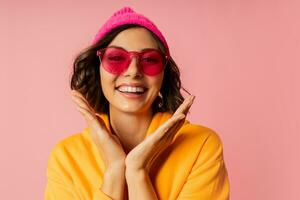 Woman in pink hat and  orange hoodie  with emotional face posing on pink bacground.  Stylish sunglasses. photo