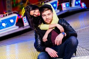 Stylish hipster  couple in love holds hands and enjoying together being in an amusement park  at night in  Odessa . Handsome man and beautiful brunette wearing trendy fall outfit. photo