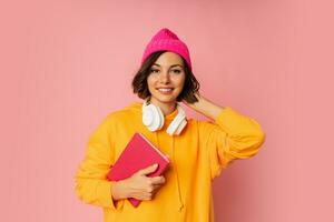 Studio photo of happy cute student with notebooks and earphones standing over pink background. Education  concept.