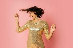 Excited  woman in elergant golden sequin dress  dancing and  enjoing new year party. Pink background. photo