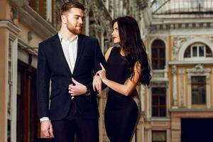 Couple in love in elegant outfit walking in old town street . Pretty brunette woman with red lips and her handsome boyfriend have time off in the evening. photo