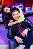 Stylish hipster  couple in love holds hands and enjoying together being in an amusement park  at night in  Odessa . Handsome man and beautiful brunette wearing trendy fall outfit. photo