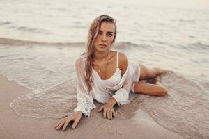 Outdoor summer portrait of beautiful happy blond woman chilling on the beach near ocean. Body care concept. photo