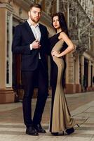 Couple in love in elegant outfit walking in old town street . Pretty brunette woman with red lips and her handsome boyfriend have time off in the evening. photo