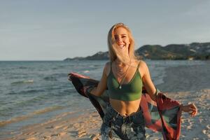 Outdoor summer image of sexy sportive blond woman posing on the beach. Wearing jeans shorts and green top. Fashion details. photo
