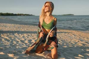 Outdoor summer image of sexy sportive blond woman posing on the beach. Wearing jeans shorts and green top. Fashion details. photo