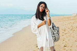 Seductive Asian woman in black top and jeans shorts , beach cover up with boho bag posing on tropical beach. Bohemian girl enjoying weekends. Perfect body.Jewelry ,bracelet and necklace. photo