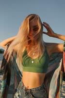 Outdoor summer image of sexy sportive blond woman posing on the beach. Wearing jeans shorts and green top. Fashion details. photo